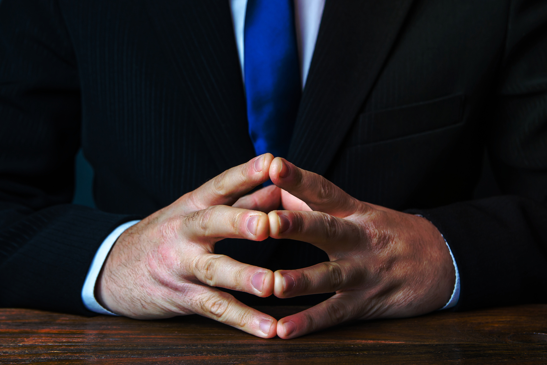 A man sits with his hands in lock. Gesture of strength consolidation and deliberation. Peace of mind and cold calculation. Conflict resolution, search for a compromise. Finding consensus. In thought